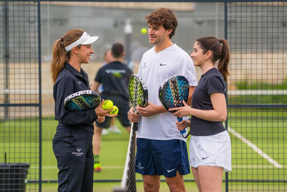 Three players on an outdoor padel court, engaged in a training session with rackets and balls.