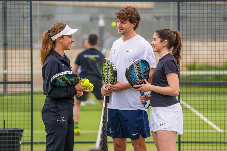 Three players on an outdoor padel court, engaged in a training session with rackets and balls.